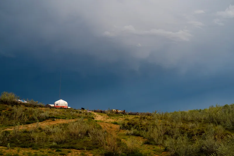 White yurt on a scrubby hillside under a dark storm sky