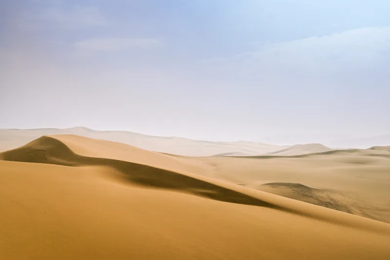 Golden sand dunes rolling toward a pale hazy horizon