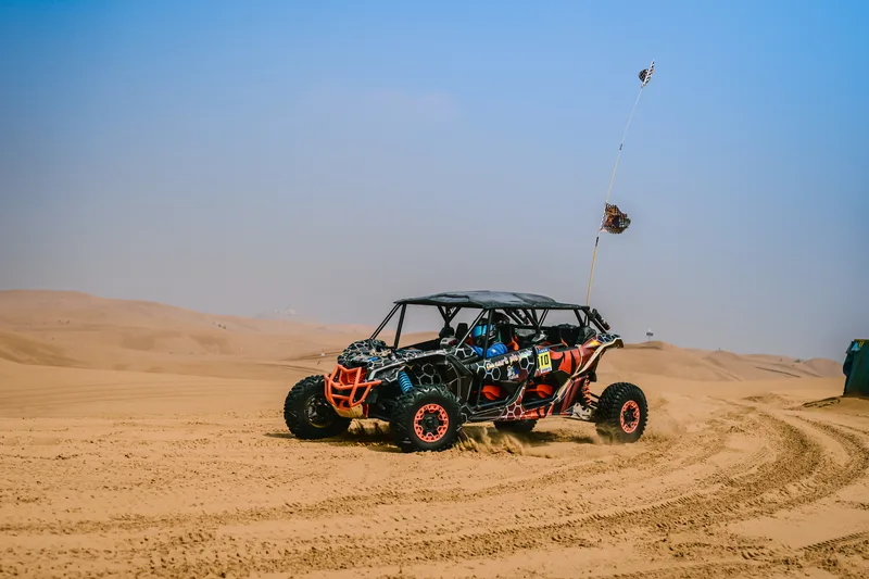 Off-road buggy churning sand across pale dunes under haze